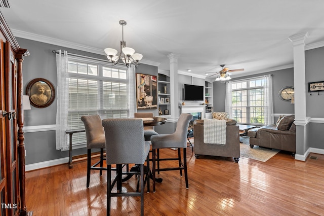 dining space with decorative columns, baseboards, wood-type flooring, ceiling fan with notable chandelier, and ornamental molding