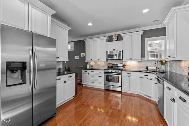 kitchen featuring a sink, appliances with stainless steel finishes, dark countertops, and ornamental molding