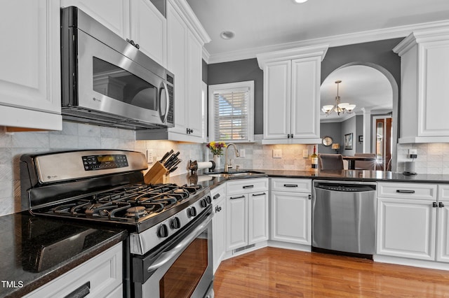 kitchen with appliances with stainless steel finishes, an inviting chandelier, a sink, arched walkways, and ornamental molding