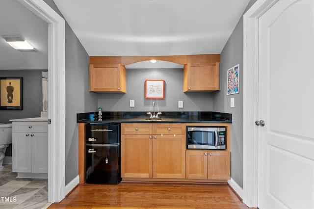 kitchen with refrigerator, dark countertops, baseboards, stainless steel microwave, and light wood-style flooring