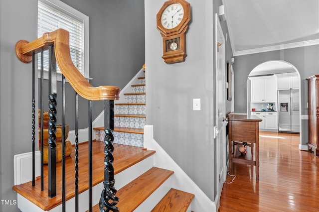 staircase featuring arched walkways, ornamental molding, baseboards, and wood finished floors