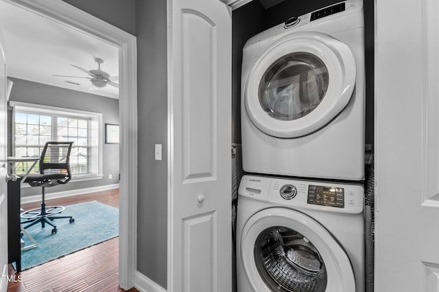 laundry room featuring laundry area, a ceiling fan, wood finished floors, baseboards, and stacked washer and clothes dryer