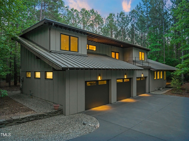 view of front of home featuring a standing seam roof, a balcony, concrete driveway, board and batten siding, and metal roof