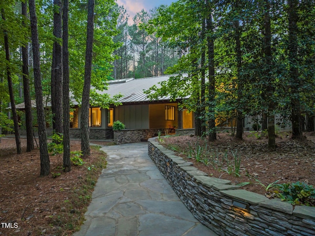 view of front of house with a standing seam roof, metal roof, stone siding, and driveway