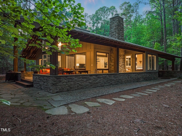 rear view of house with a chimney, stone siding, and a patio area