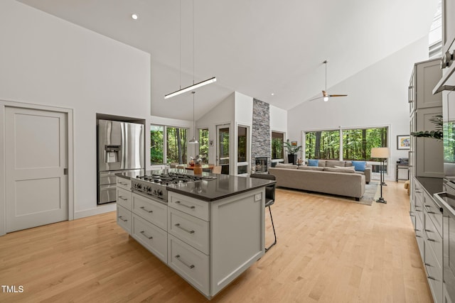 kitchen featuring appliances with stainless steel finishes, high vaulted ceiling, dark countertops, light wood finished floors, and a kitchen island