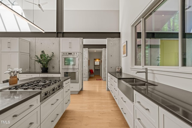 kitchen featuring appliances with stainless steel finishes, a sink, dark countertops, light wood finished floors, and white cabinets
