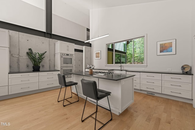 kitchen featuring stainless steel double oven, white cabinets, dark countertops, a breakfast bar area, and gas stovetop