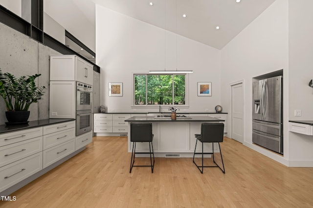 kitchen with stainless steel appliances, high vaulted ceiling, dark countertops, a breakfast bar area, and light wood-type flooring