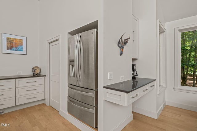 kitchen featuring stainless steel refrigerator with ice dispenser, light wood finished floors, dark countertops, white cabinetry, and baseboards