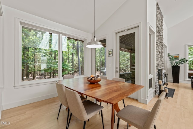dining area featuring light wood-style floors, high vaulted ceiling, baseboards, and a fireplace