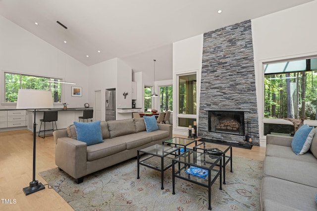 living room with high vaulted ceiling, light wood finished floors, a large fireplace, and recessed lighting