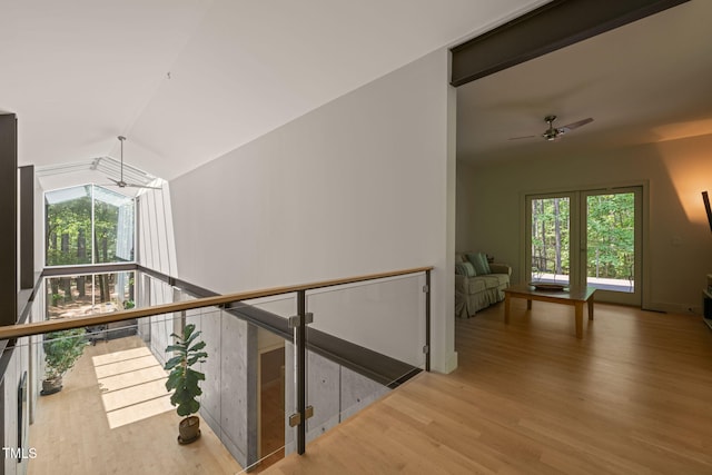corridor with wood finished floors, plenty of natural light, lofted ceiling, and an upstairs landing