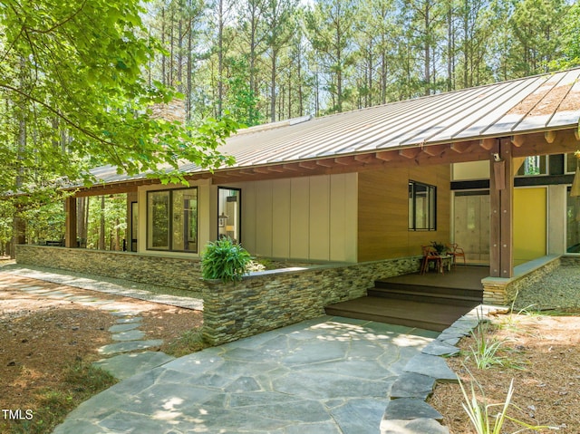 view of side of property featuring a standing seam roof, metal roof, stone siding, and an attached carport