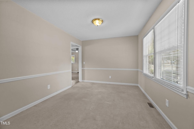 empty room with baseboards, visible vents, and light carpet