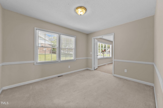 spare room with carpet floors, baseboards, a textured ceiling, and visible vents