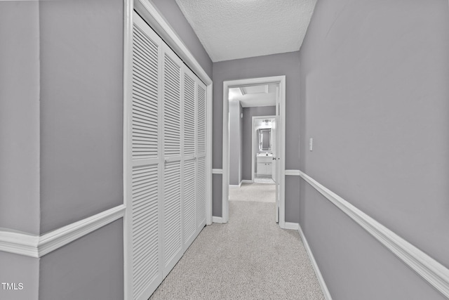 hall with baseboards, a textured ceiling, and light carpet
