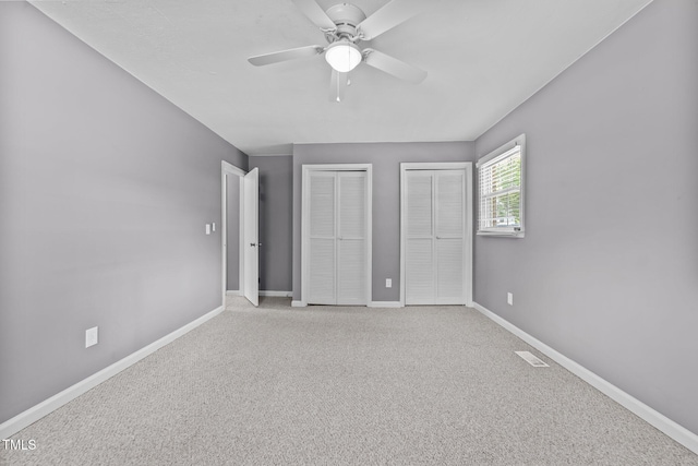 unfurnished bedroom with ceiling fan, visible vents, baseboards, multiple closets, and carpet flooring