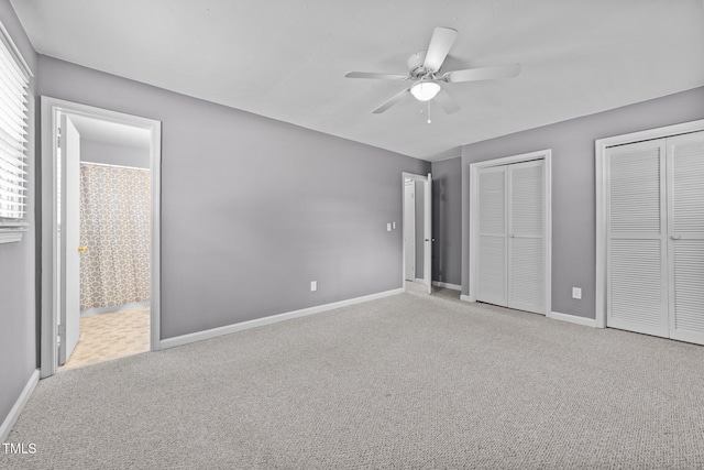 unfurnished bedroom with baseboards, a ceiling fan, carpet, and two closets