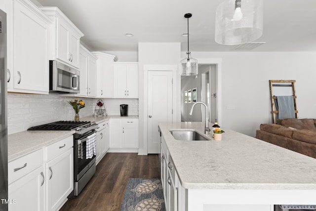 kitchen featuring appliances with stainless steel finishes, a sink, an island with sink, backsplash, and dark wood-style floors