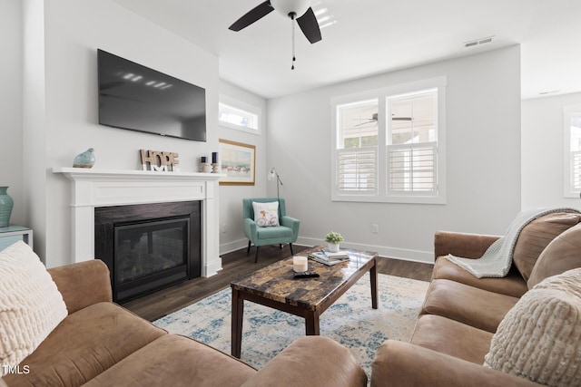 living area with ceiling fan, a glass covered fireplace, baseboards, wood finished floors, and visible vents