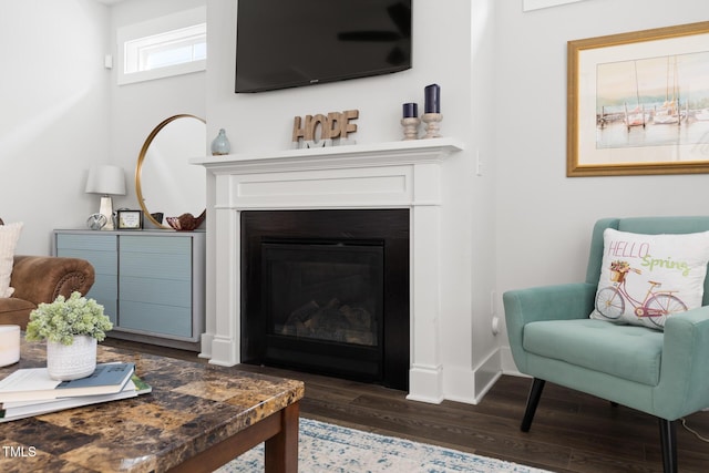 living area featuring a glass covered fireplace, baseboards, and dark wood-style floors