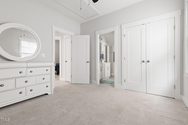 unfurnished bedroom featuring a ceiling fan, attic access, light colored carpet, a closet, and ensuite bathroom