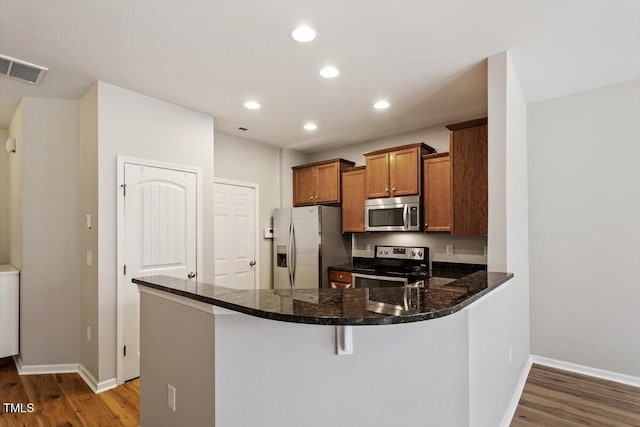 107 Tuftin Dr, Durham, NC 27703 - kitchen with appliances with stainless steel finishes, dark wood finished floors, a peninsula, brown cabinets, and recessed lighting