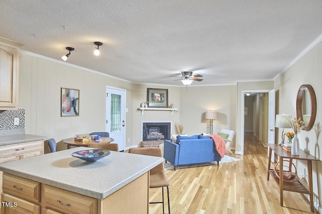 kitchen with crown molding, light wood-style floors, ceiling fan, and a fireplace