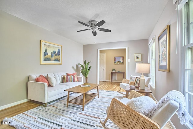 living room with baseboards, a textured ceiling, light wood finished floors, and ceiling fan