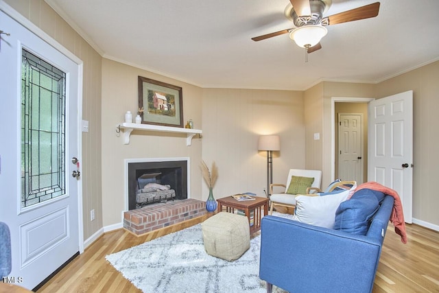 living room with crown molding, a brick fireplace, ceiling fan, and wood finished floors