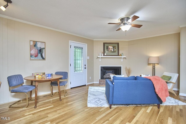 living room featuring ceiling fan, a brick fireplace, baseboards, light wood finished floors, and ornamental molding