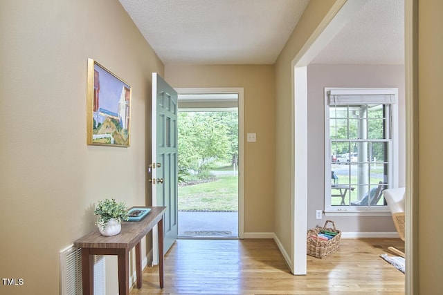 doorway to outside featuring a textured ceiling, baseboards, and light wood finished floors