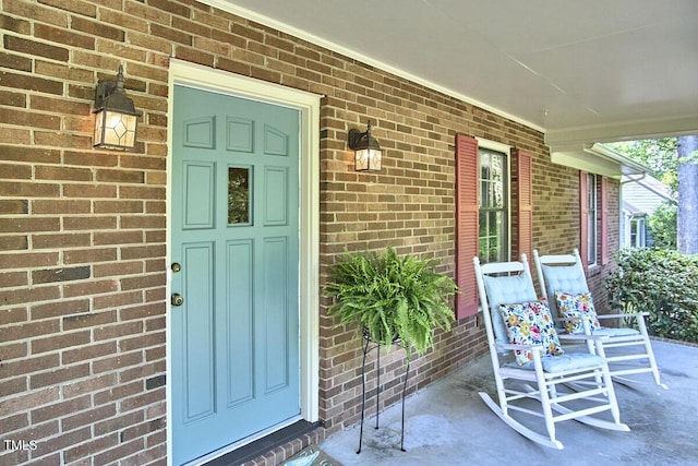 view of exterior entry featuring a porch and brick siding