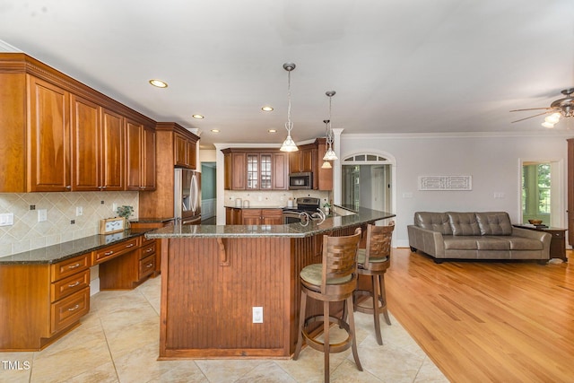 8840 Woodyhill Rd, Raleigh, NC 27613 - kitchen with appliances with stainless steel finishes, brown cabinets, a kitchen breakfast bar, crown molding, and dark stone countertops