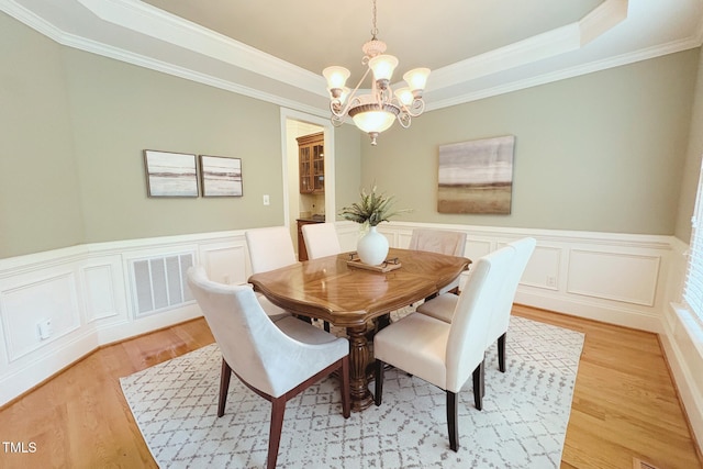 8840 Woodyhill Rd, Raleigh, NC 27613 - dining room with a chandelier, light wood-type flooring, a raised ceiling, ornamental molding, and a decorative wall
