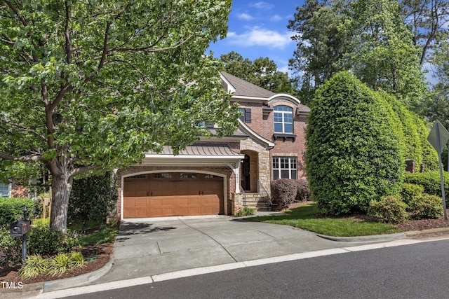 traditional-style home with a standing seam roof, driveway, brick siding, an attached garage, and stone siding