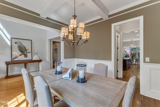 dining area featuring a wainscoted wall, light wood-type flooring, beam ceiling, and a chandelier