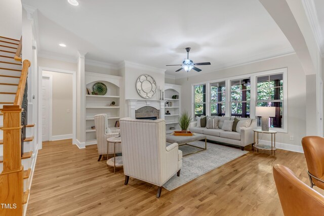 living room featuring crown molding, a ceiling fan, stairway, and a fireplace