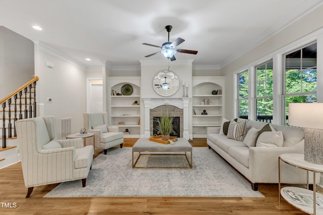 living area with crown molding, visible vents, stairs, a glass covered fireplace, and ceiling fan