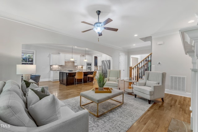 living room with a ceiling fan, visible vents, arched walkways, baseboards, and ornamental molding