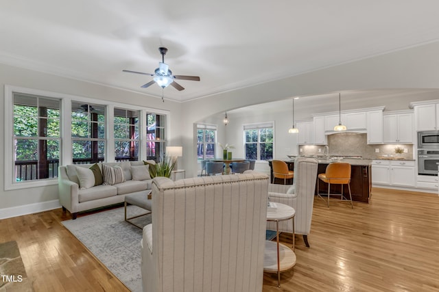 living area with light wood-type flooring, arched walkways, baseboards, and ceiling fan
