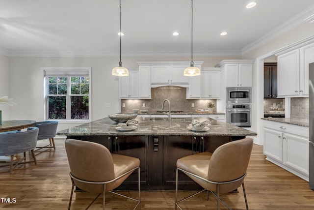 kitchen with a kitchen island with sink, tasteful backsplash, a breakfast bar, stainless steel appliances, and white cabinetry