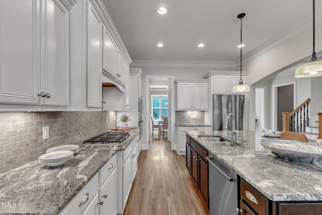 kitchen with white cabinets, appliances with stainless steel finishes, a sink, a kitchen island with sink, and tasteful backsplash