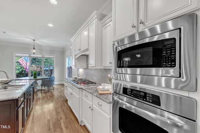 kitchen featuring crown molding, light wood-type flooring, white cabinets, a sink, and appliances with stainless steel finishes