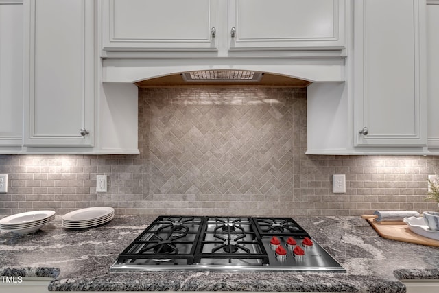 kitchen with stainless steel gas stovetop, dark stone counters, tasteful backsplash, and white cabinetry