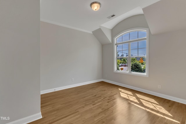 spare room featuring baseboards, wood finished floors, visible vents, and vaulted ceiling