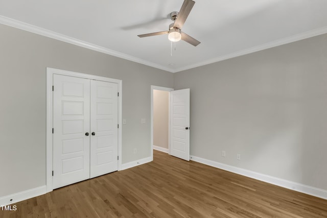 unfurnished bedroom featuring crown molding, a closet, wood finished floors, baseboards, and ceiling fan