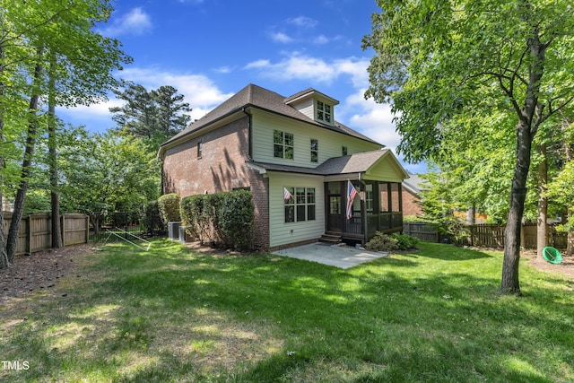 rear view of house with a sunroom, a patio area, brick siding, a fenced backyard, and a yard