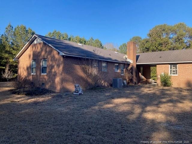 back of property with central air condition unit, a chimney, and brick siding